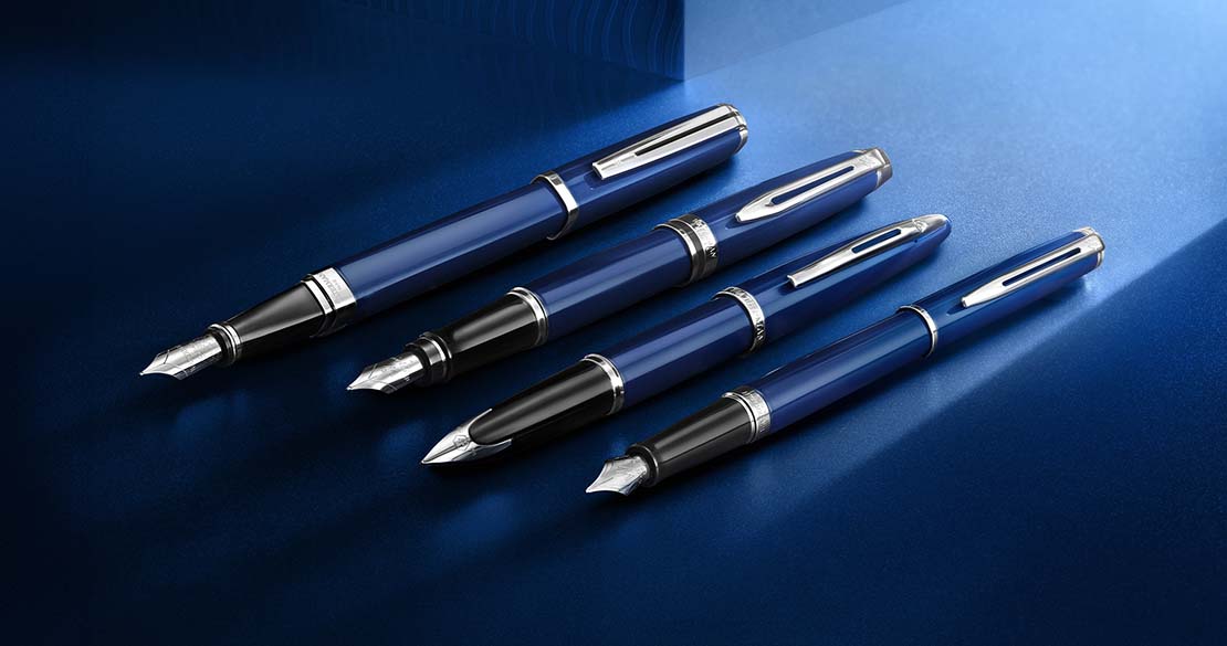 Ekskluzywne pióra i długopisy Waterman w granatowej kolorystyce z chromowanymi detalami, zaprezentowane na eleganckim, niebieskim tle.